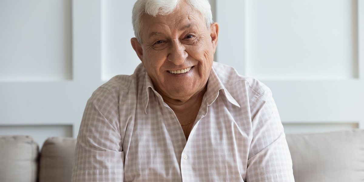 headshot portrait of smiling mature man relaxing on sofa